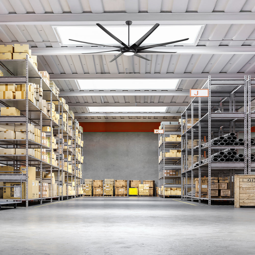 Large black ceiling fan with integrated LED light installed in a warehouse storage area